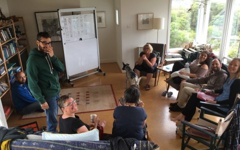 A group of Open Food Network team members sitting in a circle with a whiteboard, working together